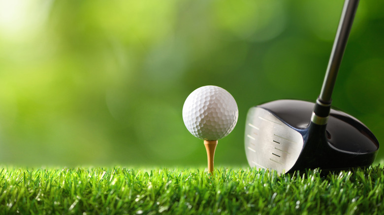 white golf ball on a tee with the head of a driver next to it