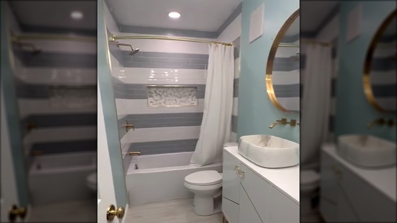 Small bathroom with blue walls and a shower with white and gray striped tiles