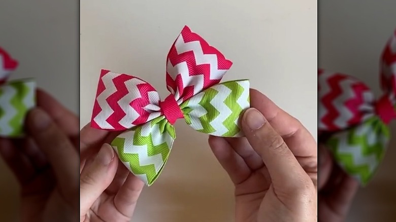 Person holding a pink and green bow they made from scrap ribbon