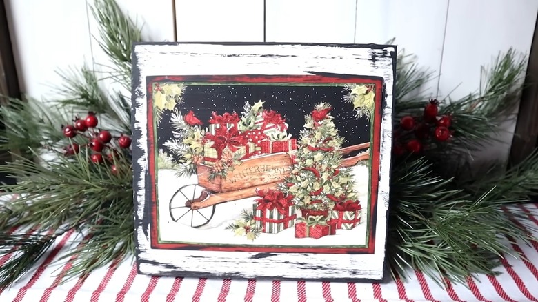 Distressed wooden sign displaying a Christmas tree and barrel full of gifts