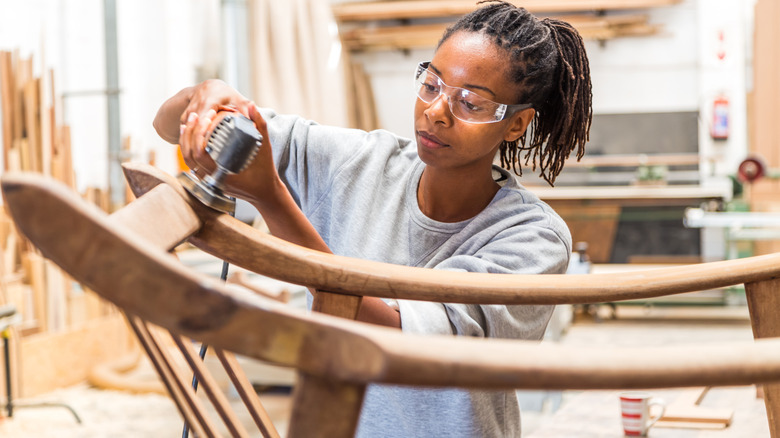 Woman using a hand saw to craft a wood furniture piece