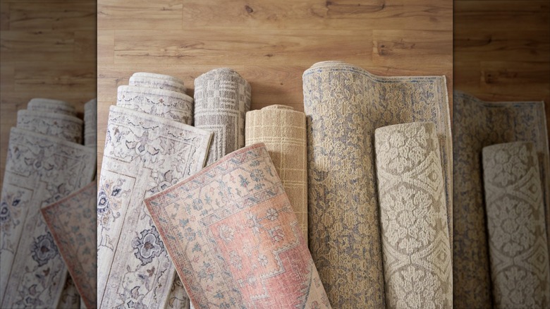 Several rolled rugs are piled on a wood floor