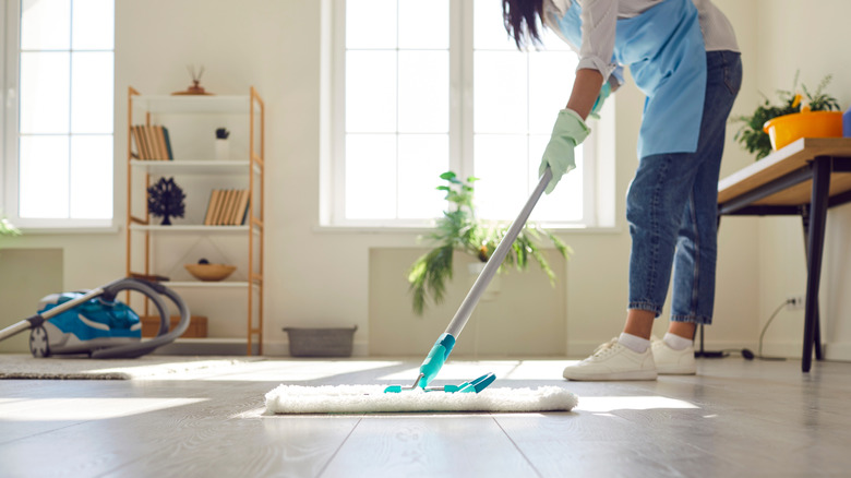 Woman mops the wood floor in a house