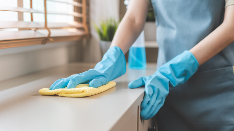 Gloved hand wiping down countertop with yellow cloth