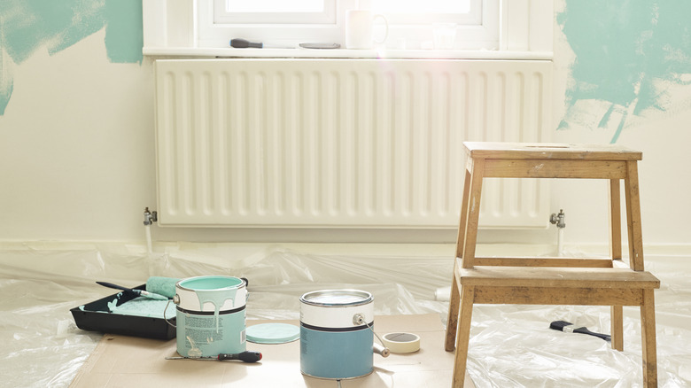 Two cans of paint in an open room, with teal paint started on the wall and a wooden stepstool on the side