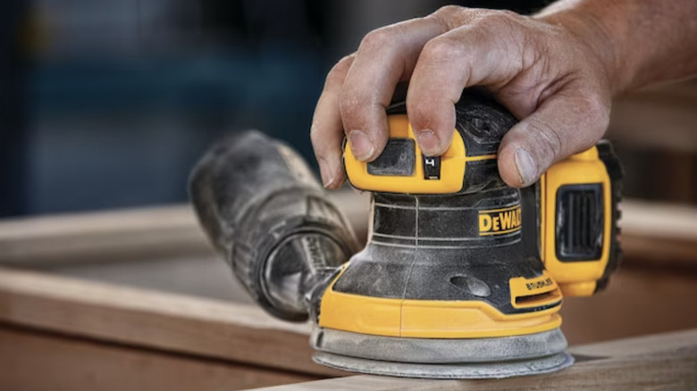 Person using a DeWalt Cordless Orbital Sander on a wood surface