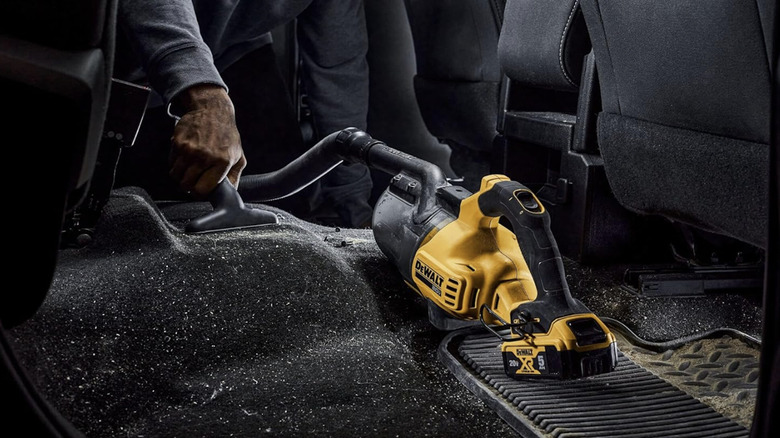 Person using a DeWalt Cordless Vacuum to clean the black interior of a car