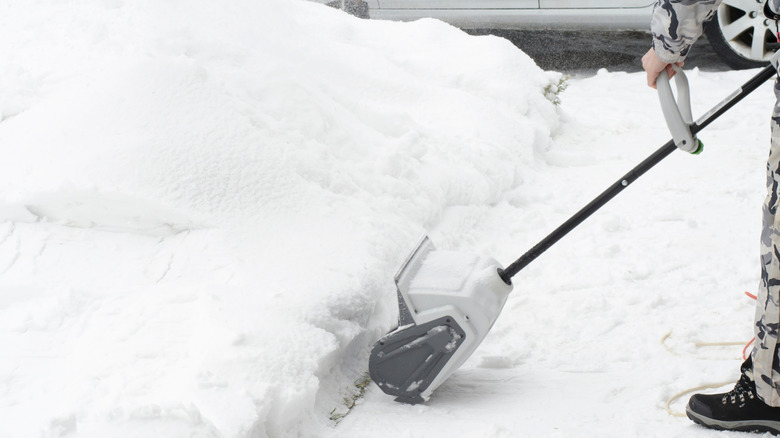 person's boot and leg and electric snow shovel removing several inches of snow