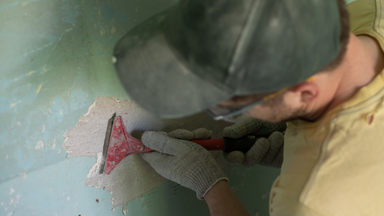 Man scraping paint from wall