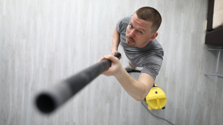 A person stretching a vacuum wand to vacuum the ceiling