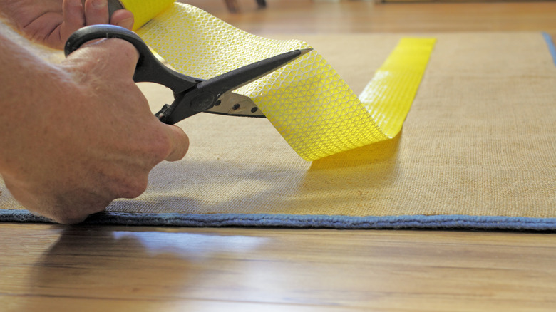 Person cutting tape on rug