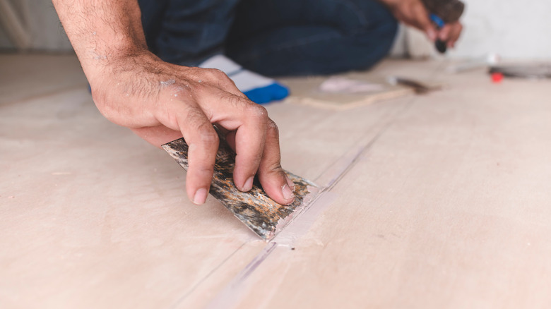 Man filling a crack in floor with wood filler