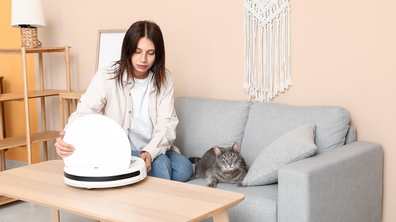 woman opening robot vacuum with cat