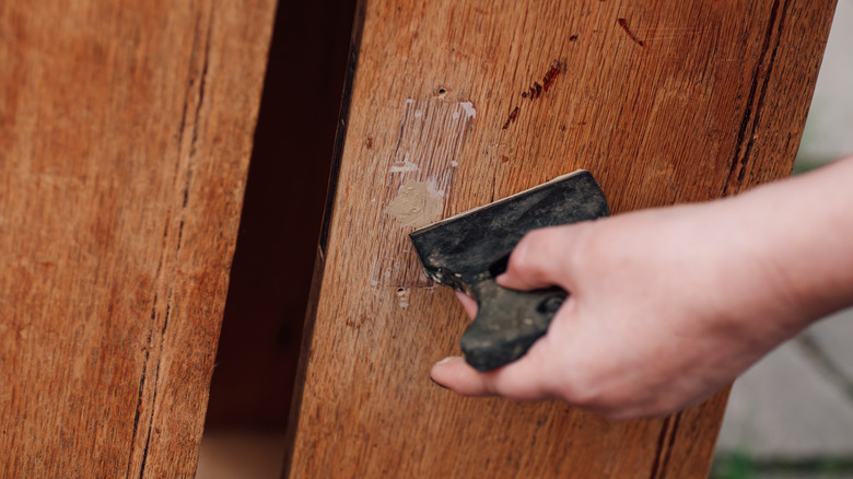 A person filling in a dent with wood putty