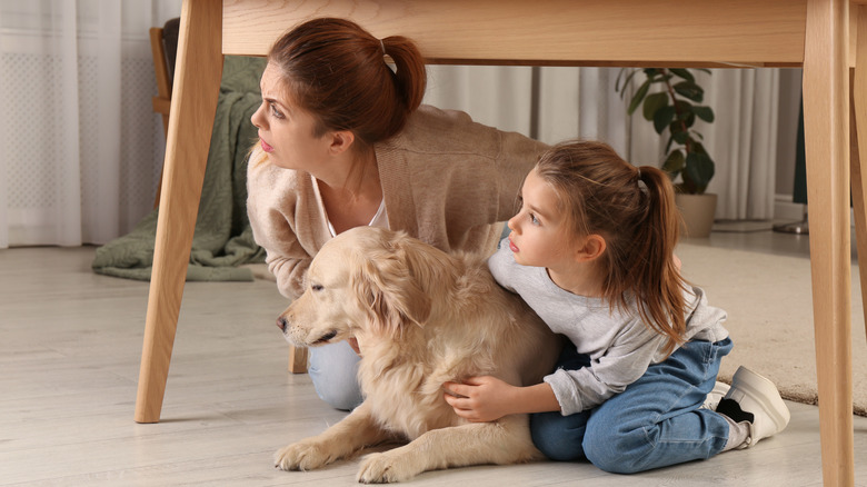 Woman, young girl, and dog hiding under a table