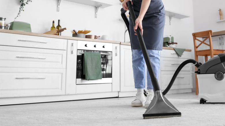 Person vacuuming carpeted floor in kitchen