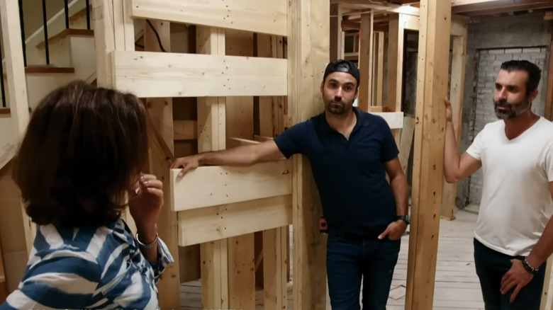 Hilary Farr standing in un-insulated post and beam room with 2 contractors