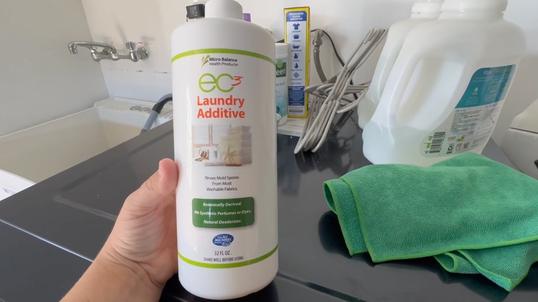 Person holding a bottle of EC3 Laundry Additive by a laundry machine