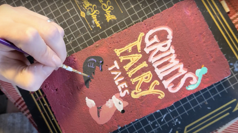 person painting detailed book cover on brick