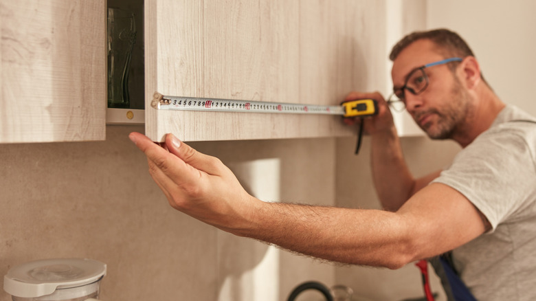 A man measures light colored kitchen cabinets