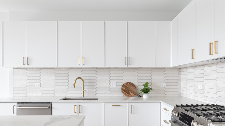 White cabinets in white kitchen with tile backsplash and small plant