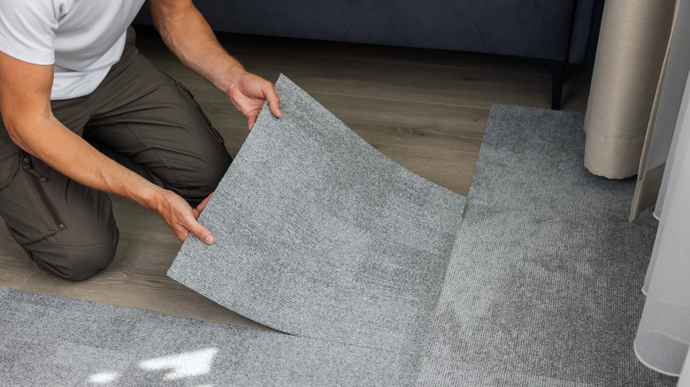 Man kneeling on floor installing gray carpet square