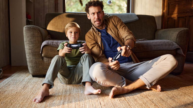 Dad and son playing video game while sitting on carpeted floor