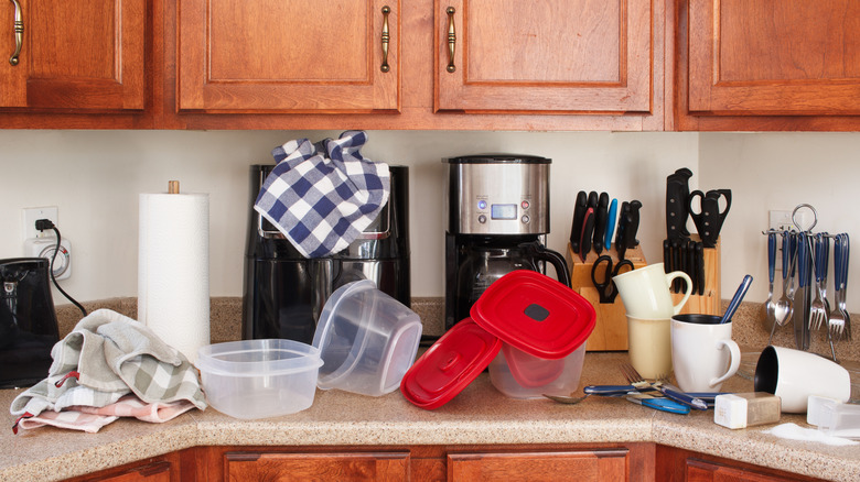 A traditional style kitchen with wooden cabinets and clutter on countertop, including scattered food containers and dishcloths.