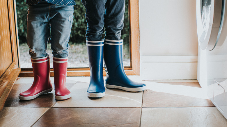 Two children in boots standing in the doorway of a room with beige checkerboard tile floors