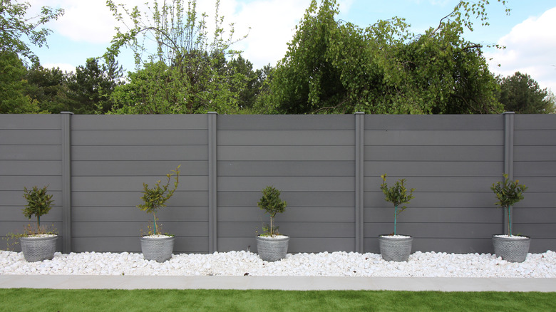 grey wood composite fence with plants in front and trees in the background