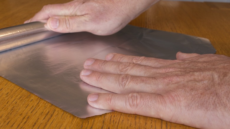 Hands unrolling aluminum foil