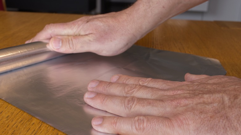 Hands rolling out aluminum foil