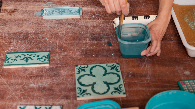 Person painting turquoise tile on wooden surface