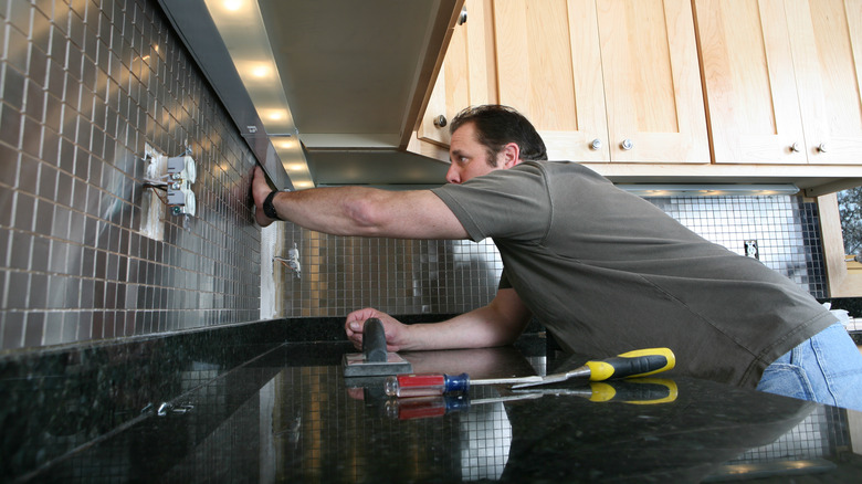 person installing metal tile backsplash