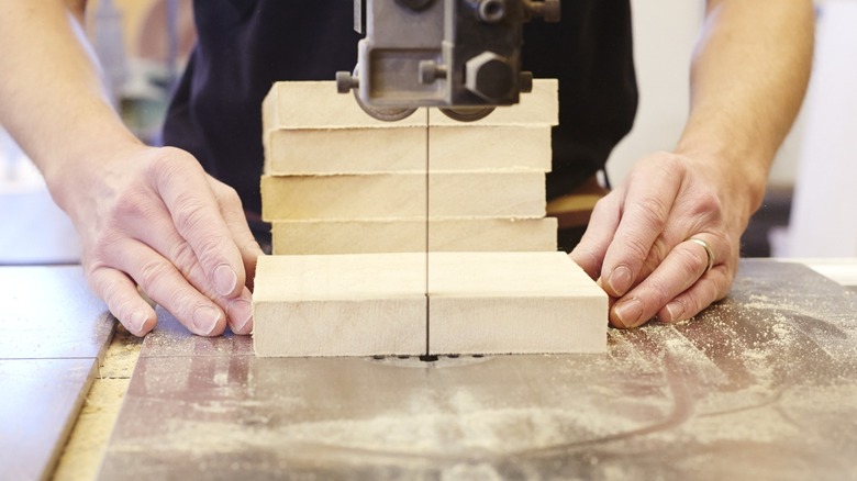 man cutting wood block in half with bandsaw