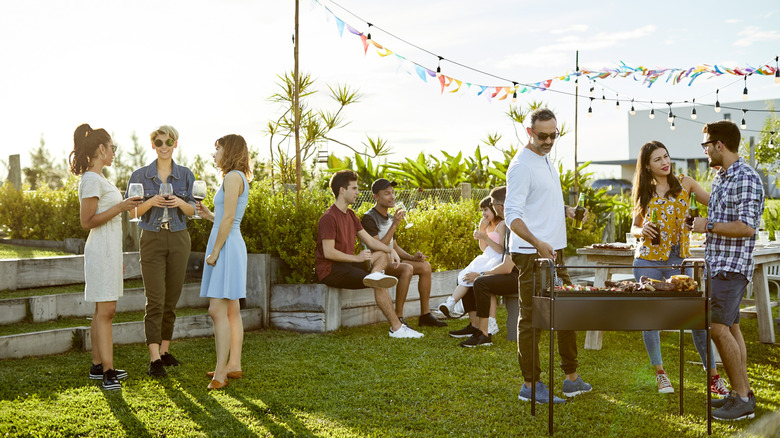 Several groups of casually dressed people chat at a backyard gathering