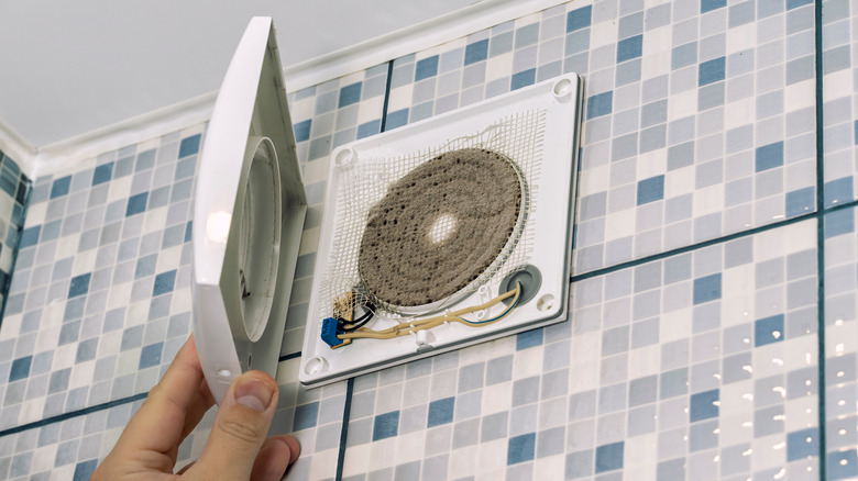 A person removing the cover from a dirty extractor fan in a bathroom