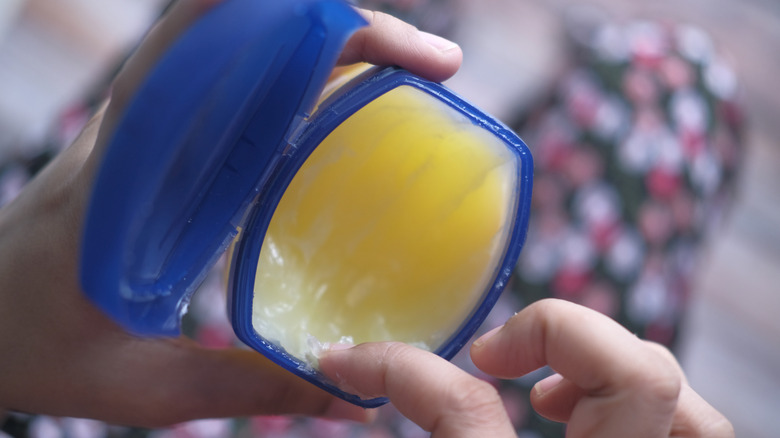 A person scoops Vaseline out of a tub with their finger.