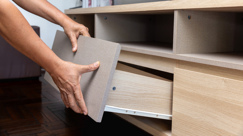 A person's hands pull a drawer out of a furniture cabinet