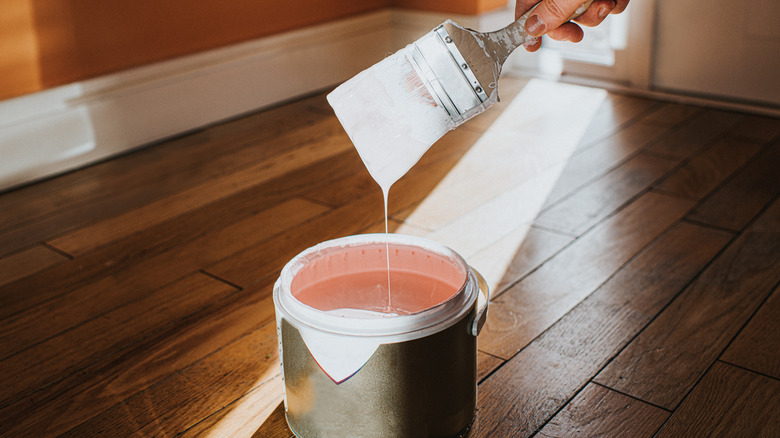 Can of paint and wet brush in the middle of wood flooring