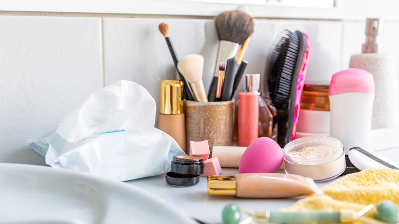 A messy pile of makeup on the bathroom counter