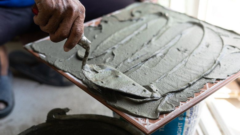 Person smoothing adhesive on the back of a large tile