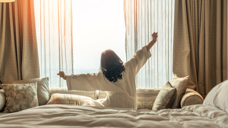 Woman stretches in bed next to open window