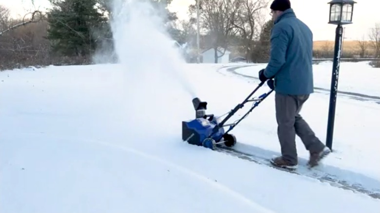 a person using the Snow Joe Snow Blower to clear a sidewalk near a lamp post