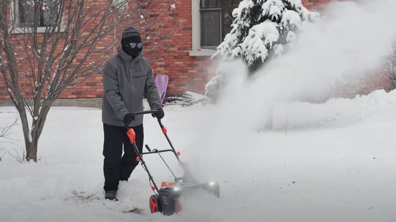 Person in front of brick house using the VOLTASK Snow Blower