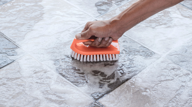 Person cleaning tile floor with an orange brush