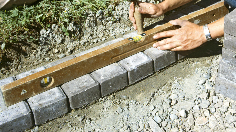 man laying paver stone edging over gravel