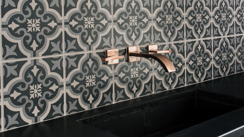 Patterned backsplash tiles with a black sink and copper faucet