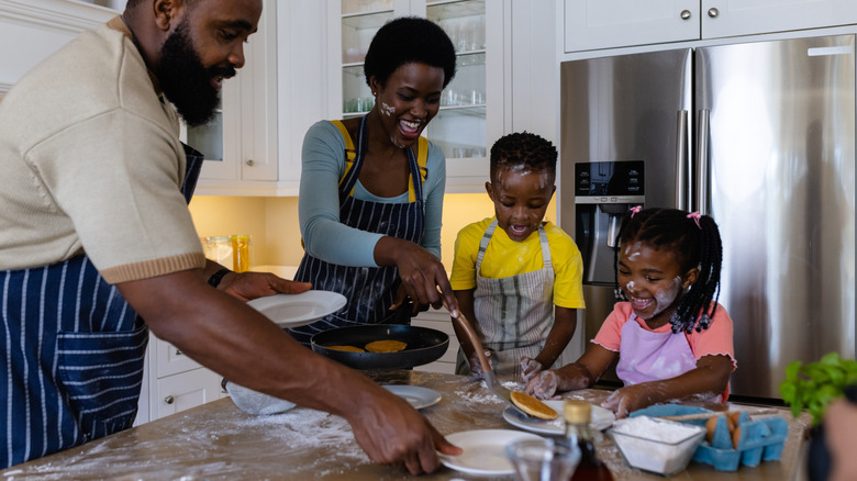 family having pancakes and flour is scattered on them and the kitchen countertop