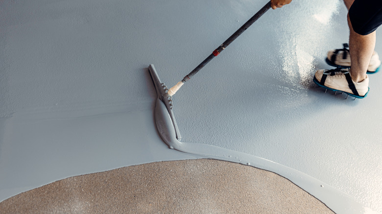 Person applying epoxy garage floor coating with squeegee